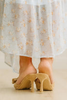 Beige high-heeled shoes worn with a light-colored floral dress.