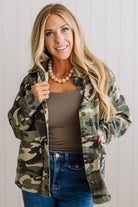 Blonde woman wearing a camo lightweight jacket in a light walled studio.