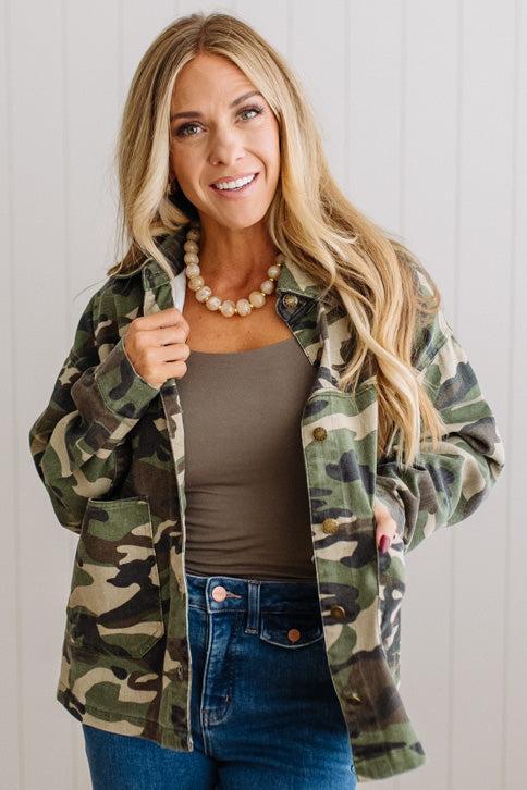 Blonde woman wearing a camo lightweight jacket in a light walled studio.