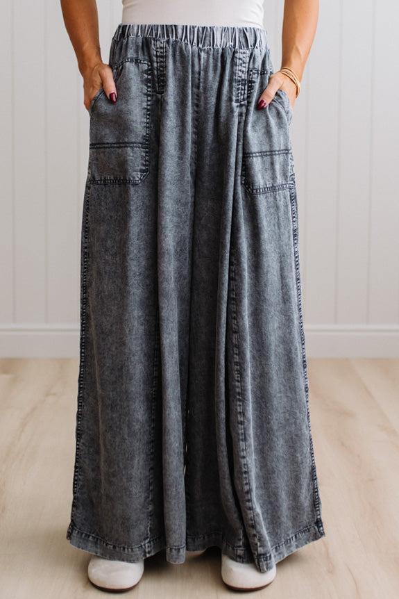 WOMAN IN A BRIGHTLY LIT STUDIO WEARING A TANK WITH CHAMBRAY ELASTIC WAIST POUCH POCKET WIDE LEG CULOTES PANTS IN GREY.