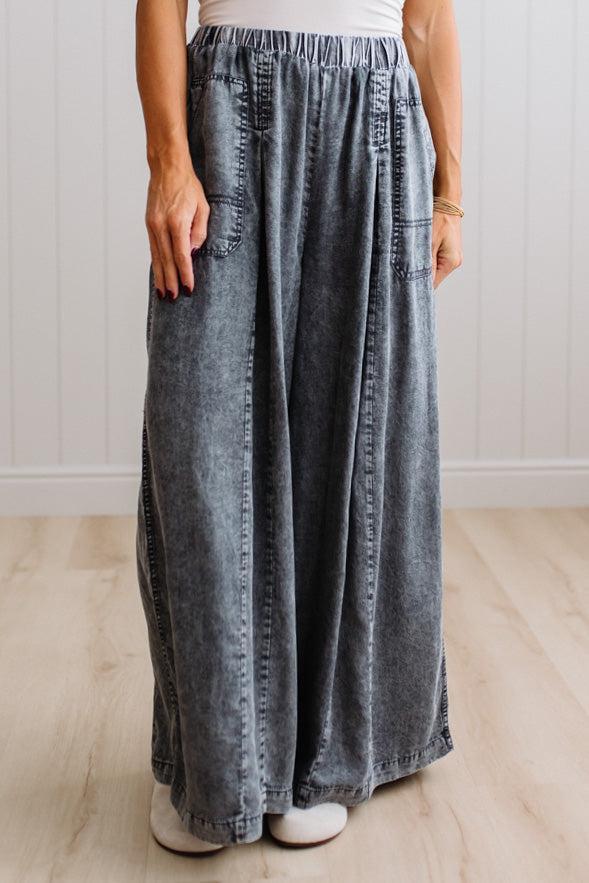 WOMAN IN A BRIGHTLY LIT STUDIO WEARING A TANK WITH CHAMBRAY ELASTIC WAIST POUCH POCKET WIDE LEG CULOTES PANTS IN GREY.