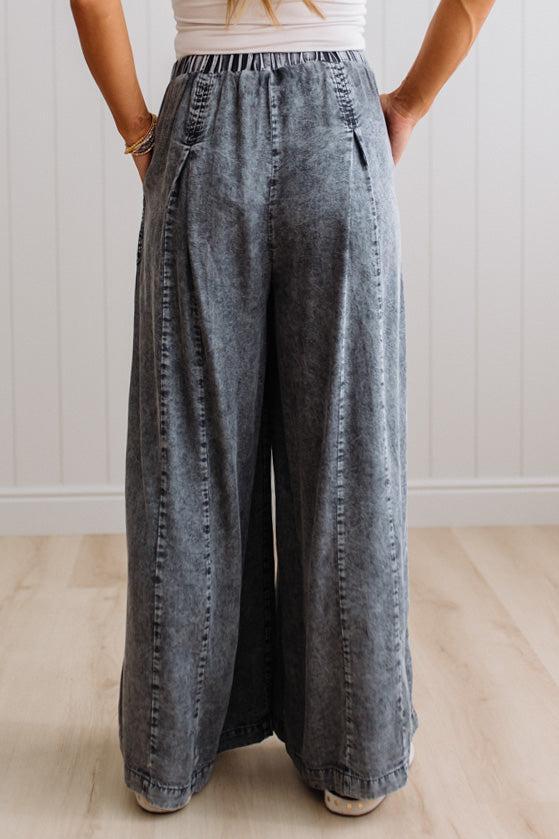 WOMAN IN A BRIGHTLY LIT STUDIO WEARING A TANK WITH CHAMBRAY ELASTIC WAIST POUCH POCKET WIDE LEG CULOTES PANTS IN GREY.