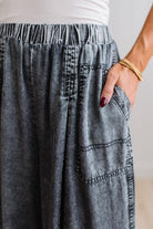 WOMAN IN A BRIGHTLY LIT STUDIO WEARING A TANK WITH CHAMBRAY ELASTIC WAIST POUCH POCKET WIDE LEG CULOTES PANTS IN GREY.