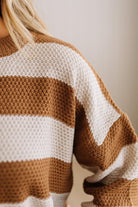 Close-up of a person wearing a chunky knit sweater with wide horizontal stripes in warm brown and off-white.