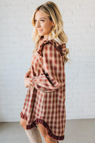 Woman wearing a plaid dress with ruffled details against a white brick wall.