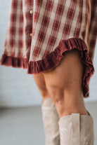 Person wearing a plaid dress with ruffled hem and beige knee-high boots on a neutral background