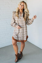 Woman wearing a plaid dress with ruffled details against a white brick wall.