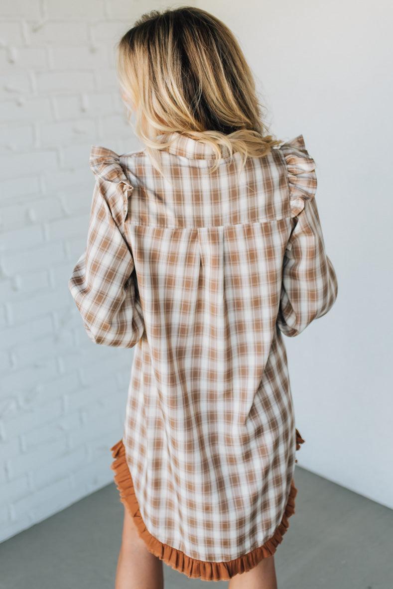 Woman wearing a plaid dress with ruffled details against a white wall.