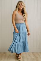 Woman wearing a striped tank top and blue tiered skirt against a neutral background