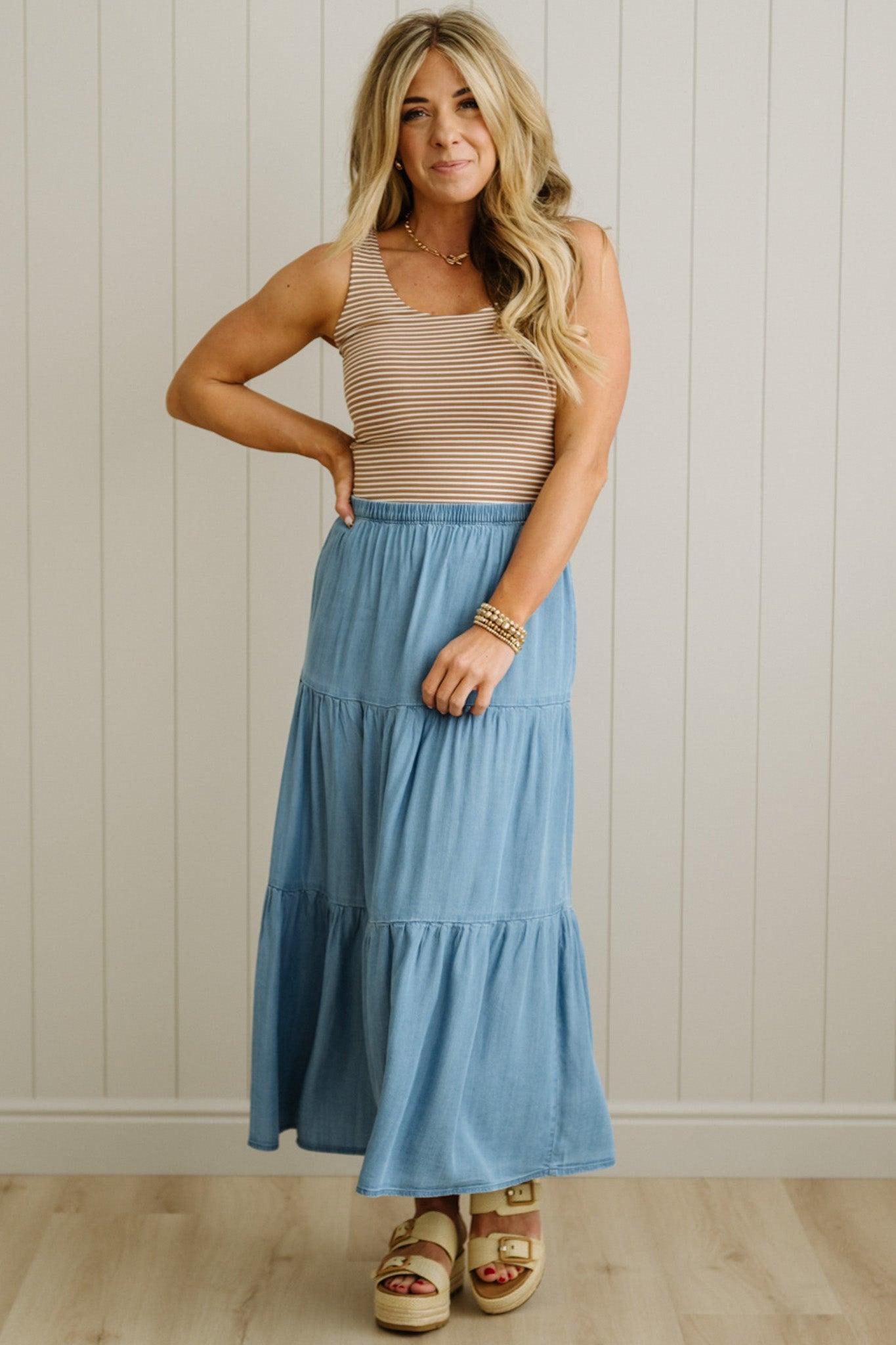Woman wearing a striped tank top and blue tiered skirt against a neutral wall.