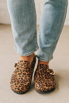 Woman wearing leopard print faux leather slip on clogs with single gold buckle on the side.
