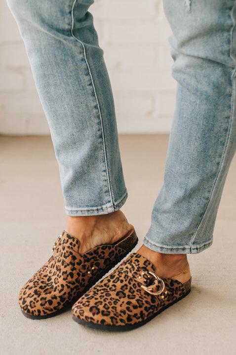 Woman wearing leopard print faux leather slip on clogs with single gold buckle on the side.