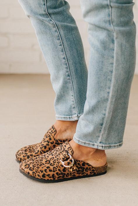 Woman wearing leopard print faux leather slip on clogs with single gold buckle on the side.