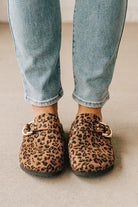 Woman wearing leopard print faux leather slip on clogs with single gold buckle on the side.