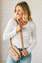 Woman holding a beige crossbody bag against a white brick wall