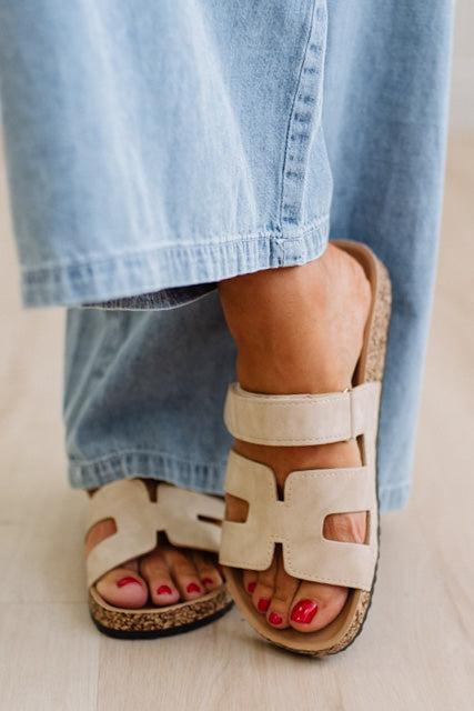 Close-up of beige sandals worn with light blue jeans on a neutral background