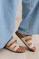 Close-up of feet wearing beige sandals with cork soles and blue jeans.