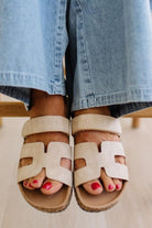 Beige sandals worn with light blue jeans on a neutral background