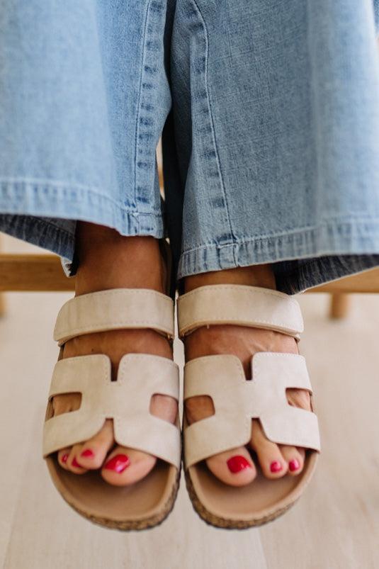 Beige sandals worn with light blue jeans on a neutral background