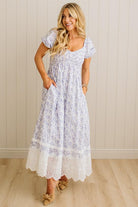 Woman wearing a white floral dress with lace details against a beige wall.