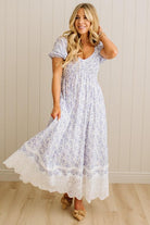 Woman wearing a white floral dress with lace trim against a beige wall.