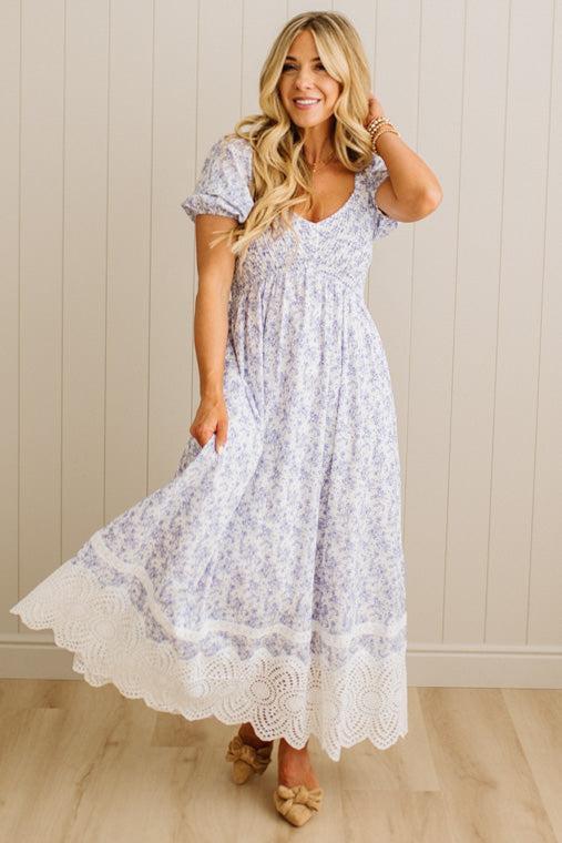 Woman wearing a white floral dress with lace trim against a beige wall.