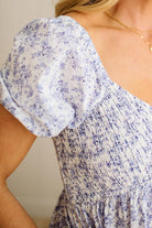 White dress with blue floral pattern and lace trim on a wooden floor.