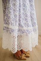 White dress with blue floral pattern and lace trim on a wooden floor.