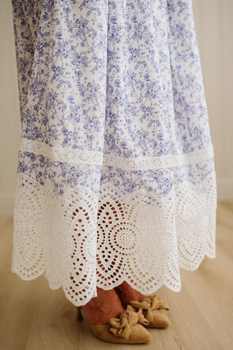 White dress with blue floral pattern and lace trim on a wooden floor.