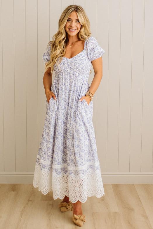 Woman wearing a floral dress with lace hem against a beige wall.