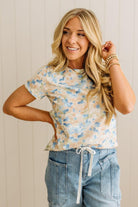 Woman wearing a floral top and denim shorts against a neutral background