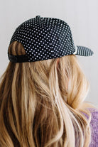 BLONDE WOMAN WEARING A BLACK AND WHITE POLKA DOT HAT WITH WHITE ROPE ACROSS THE FRONT AND A PATCH THAT SAYS JUST HAPPY TO BE HERE ON THE CENTER FRONT.