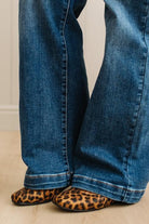 Blue jeans worn by a person with leopard print slippers on a neutral background
