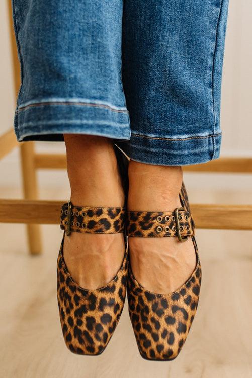 Leopard print shoes worn with rolled-up blue jeans on a blurred background