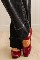 Red shoes worn with black pants on a light wooden floor.