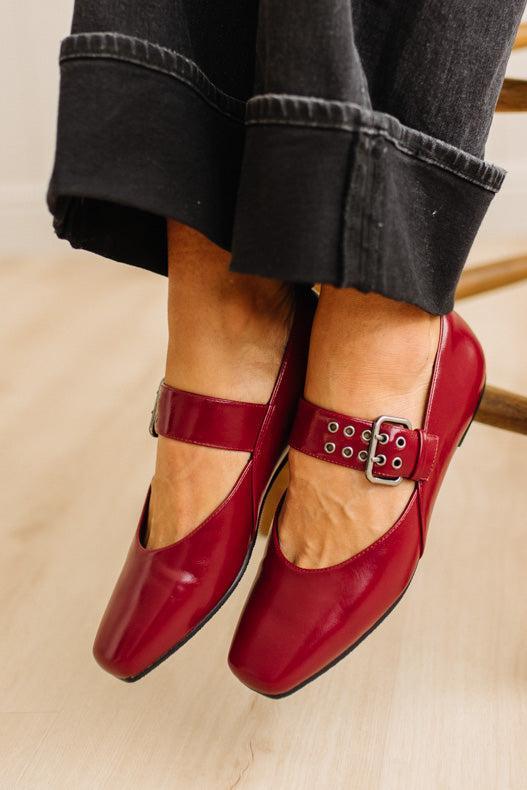 Red shoes with buckles worn with black jeans on a light background