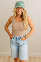 Woman wearing a striped tank top, denim shorts, and a green cap indoors.