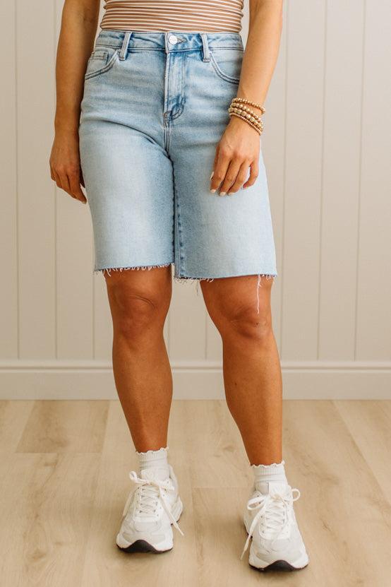 Person wearing light blue denim shorts and white sneakers on a neutral background