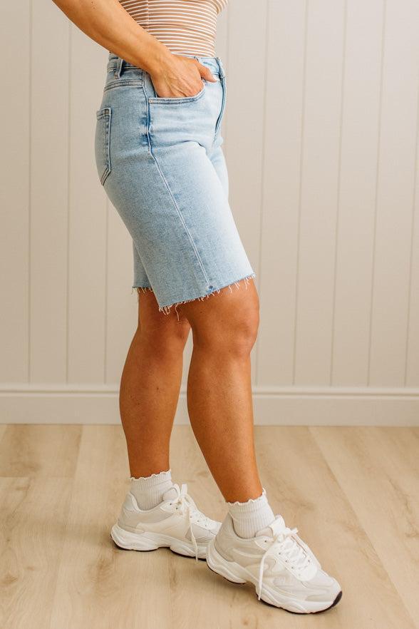 Person wearing a light blue denim skirt and white sneakers on a wooden floor.