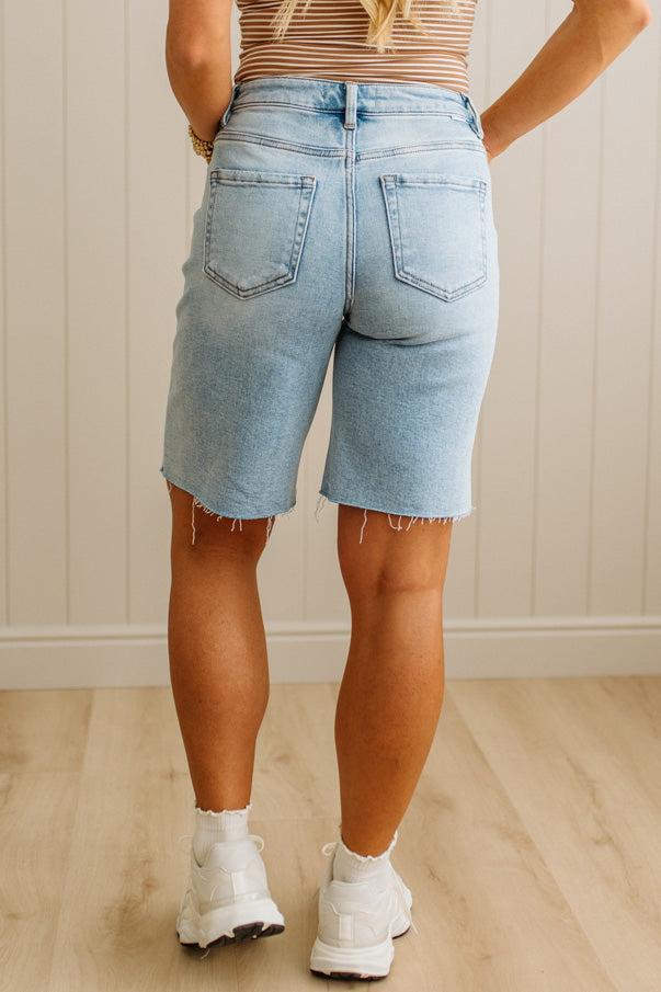 Person wearing light blue denim shorts and white sneakers in a room with wooden flooring and a neutral wall.