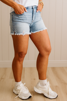 Person wearing denim shorts and white sneakers in a neutral setting