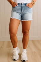 Person wearing light blue denim shorts and white sneakers against a neutral background