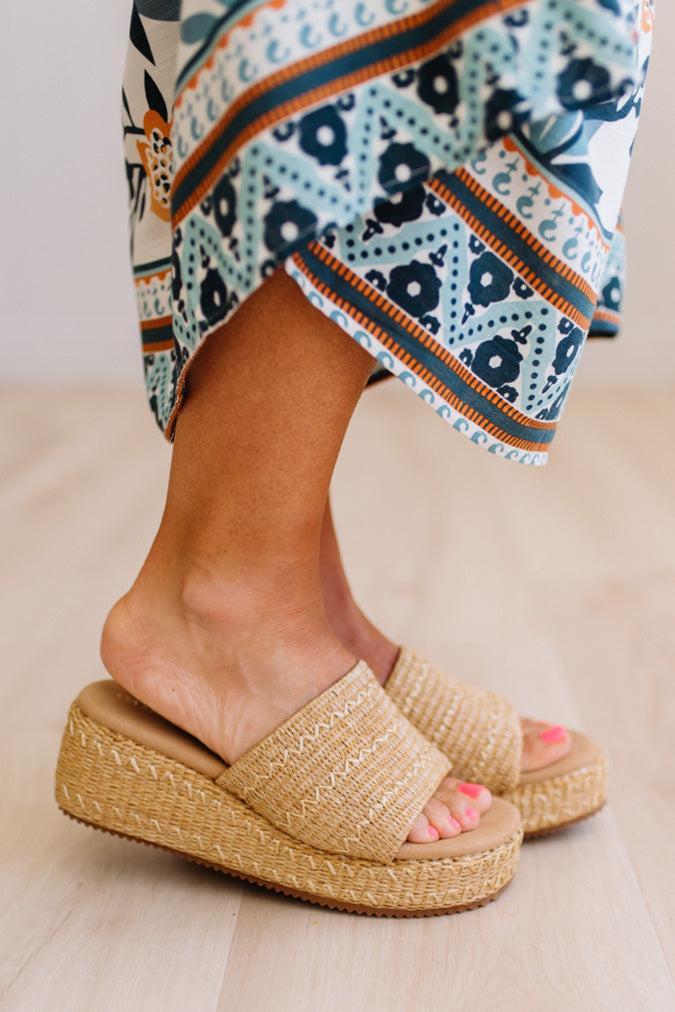 Person wearing patterned pants and brown sandals on a neutral background
