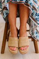 Person wearing beige sandals with a patterned dress and chair in the background