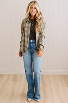 Blonde woman wearing a grey shirt with an opened olive green plaid flannel button up top over. 