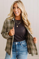 Blonde woman wearing a grey shirt with an opened olive green plaid flannel button up top over. 