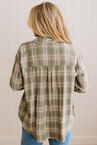 Blonde woman wearing a grey shirt with an opened olive green plaid flannel button up top over. 