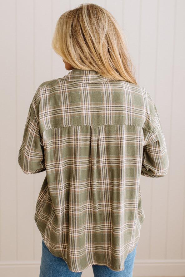 Blonde woman wearing a grey shirt with an opened olive green plaid flannel button up top over. 