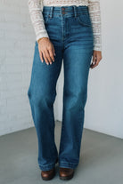 Person wearing blue jeans against a white brick wall.