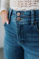 Close-up of blue jeans with brand name on buttons against a neutral background